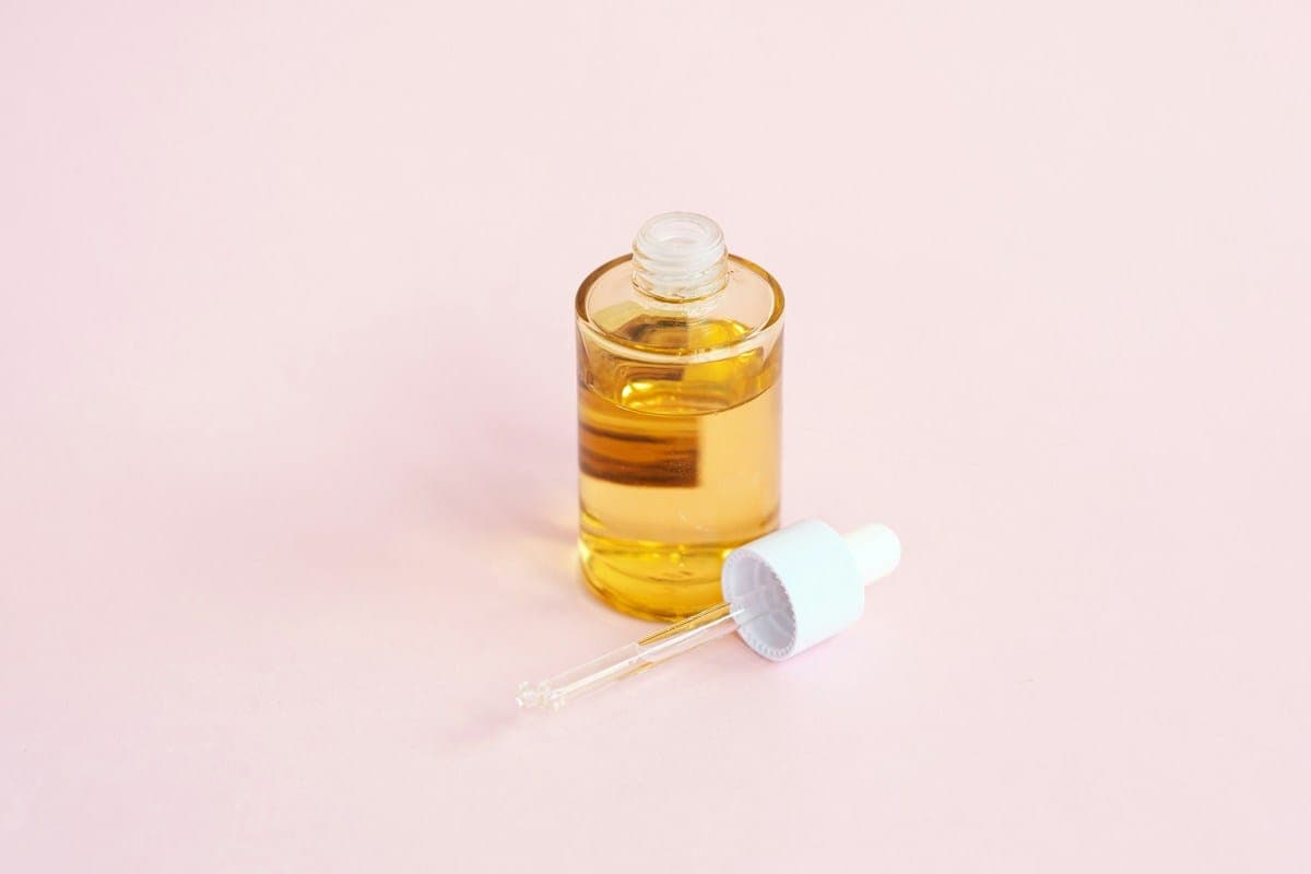 A serum bottle with a dropper on a pink surface